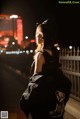 A woman in a black dress and hat standing on a bridge.