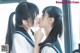 A couple of young women in school uniforms kissing each other.