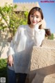 A woman in a white sweater leaning against a wall.