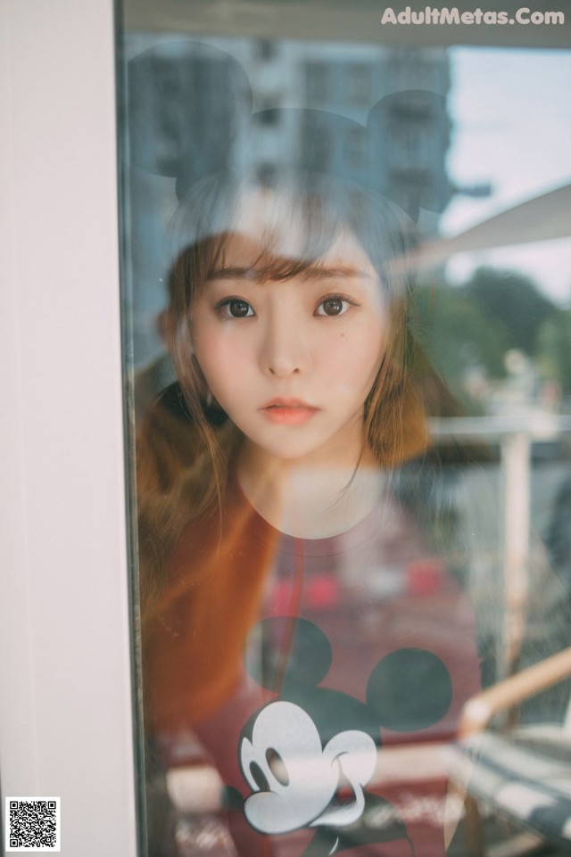 A woman looking out of a window with a mickey mouse shirt on.