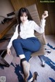 A woman sitting on a chair in a white shirt and blue pants.