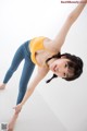 A woman in a yellow top and blue leggings doing a yoga pose.