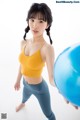 A woman in a yellow top and blue leggings holding a blue ball.