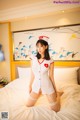 A woman dressed as a nurse sitting on a bed.