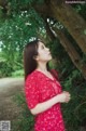 A woman in a red dress standing under a tree.