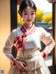 A woman in a white and red hanbok standing in front of a window.