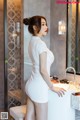 A woman in a white dress standing in front of a sink.