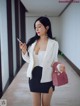 A woman in a white blazer and black skirt holding a cell phone.