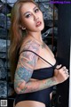 A woman with tattoos on her arms leaning against a wall.