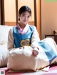 A woman in a blue and white hanbok sitting on a bed.