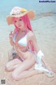 A woman in a bikini and hat sitting on the beach.