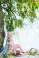 A woman sitting under a tree next to a body of water.