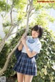 A woman in a school uniform leaning against a tree.