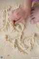 A child's hand writing in the sand on a beach.