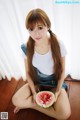 A woman sitting on the floor holding a slice of watermelon.