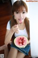 A woman eating a slice of watermelon with a spoon.