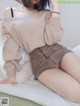 a woman sitting on top of a bed wearing a beige sweater and skirt