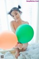 A young woman sitting in a bathtub holding two balloons.