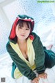 A woman in a green and yellow dinosaur costume sitting on a bed.