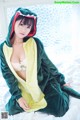 A woman in a green and yellow dinosaur costume sitting on a bed.