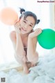 A young woman sitting on a bed holding two balloons.