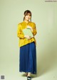 A woman in a yellow shirt and blue skirt holding a green book.