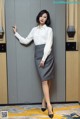 A woman in a white shirt and gray skirt posing in an elevator.