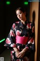 A woman in a black and pink kimono leaning against a wall.