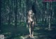 A naked woman standing in the middle of a forest.