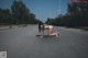 A naked woman kneeling down on the side of a road.