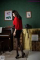 A woman in a red blouse and black skirt standing in front of a piano.