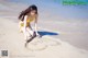 A woman in a yellow bikini drawing a heart in the sand.