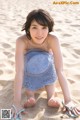 A young woman in a blue dress and flip flops on the beach.