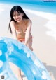 A woman in a bikini playing with an inflatable ring on the beach.