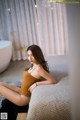 A woman in a brown bodysuit sitting on a bed.