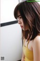 A woman in a yellow tank top looking out a window.