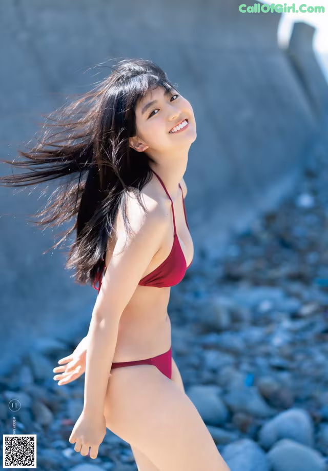 A woman in a red bikini standing on a rocky beach.