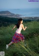 A woman in a pink tank top and plaid skirt running through tall grass.