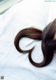 A woman with long brown hair in a ponytail laying on a bed.