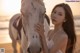 A woman standing next to a white horse on a beach.