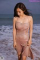 A woman in a pink dress standing on the beach.