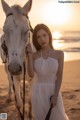 A woman in a white dress standing next to a white horse.