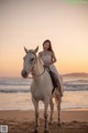 A woman in a white dress riding a white horse on the beach.