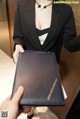 A woman in a black suit holding a black folder.